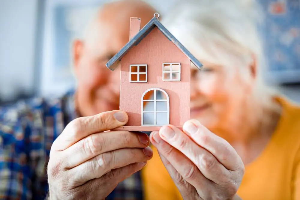 Senioren halten gemeinsam eine Figur eines kleinen Hauses in den Händen als Vorfreude auf Ihren Seniorenumzug